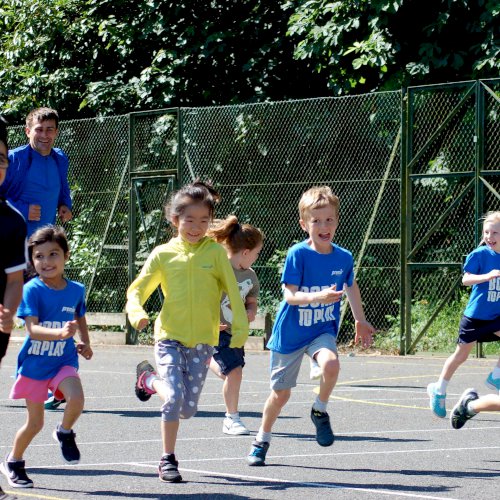 Young children running across a tennis court, smiling and having fun